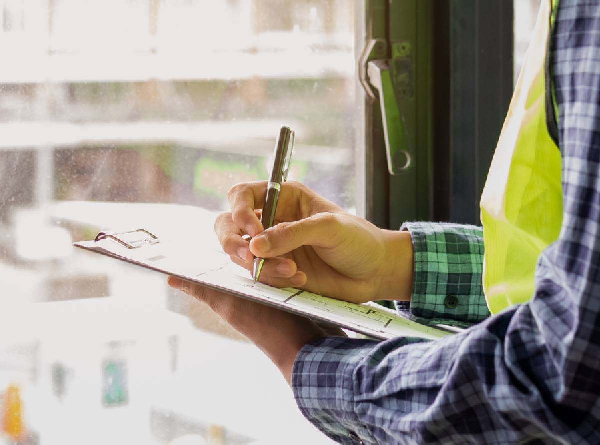 Close up of someone from shoulder down to waist, writing with a pen on a clipboard, wearing hi-vis jacket